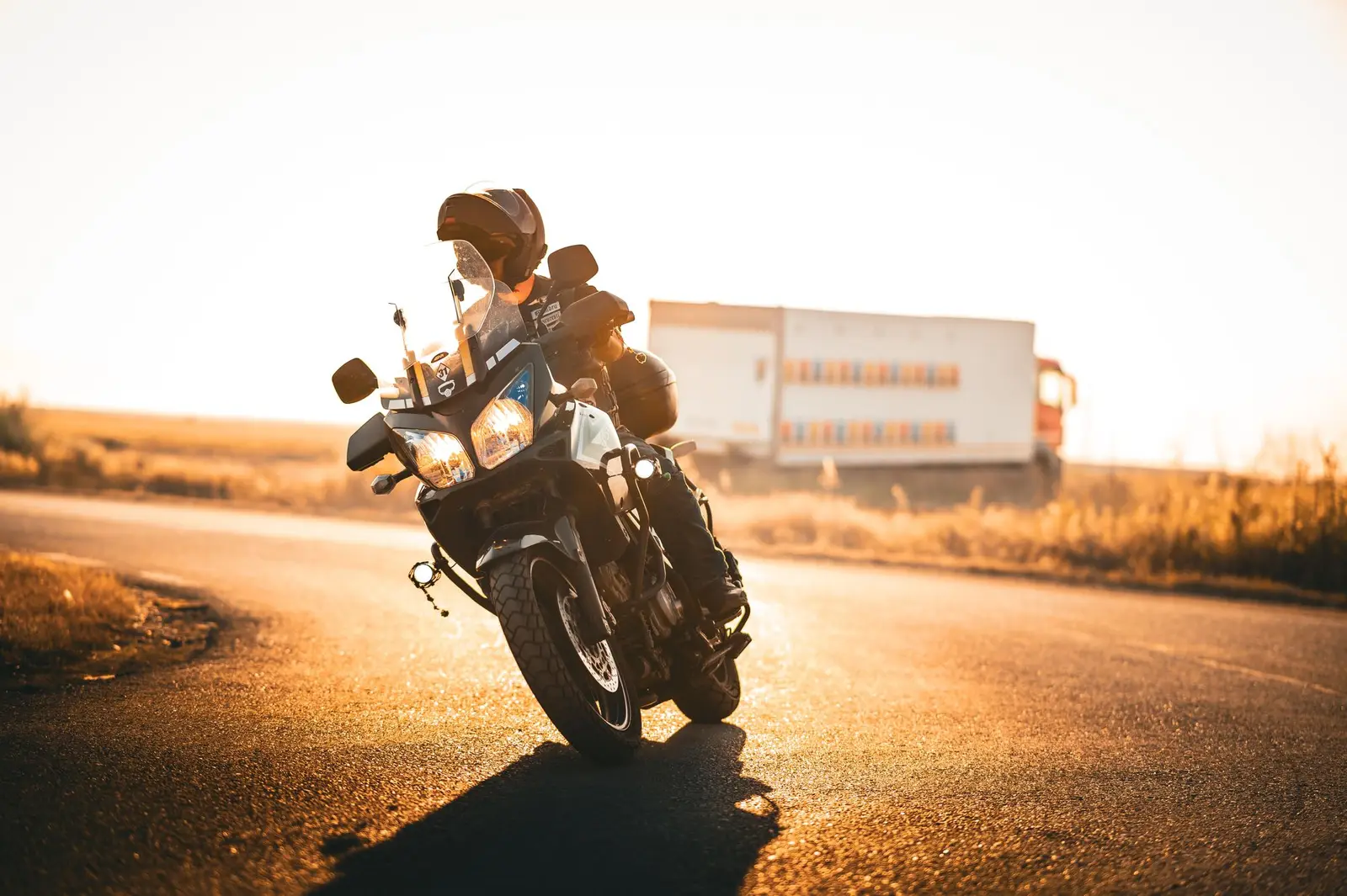 A helmeted motorcyclist riding a paved road, with a lorry in the distance