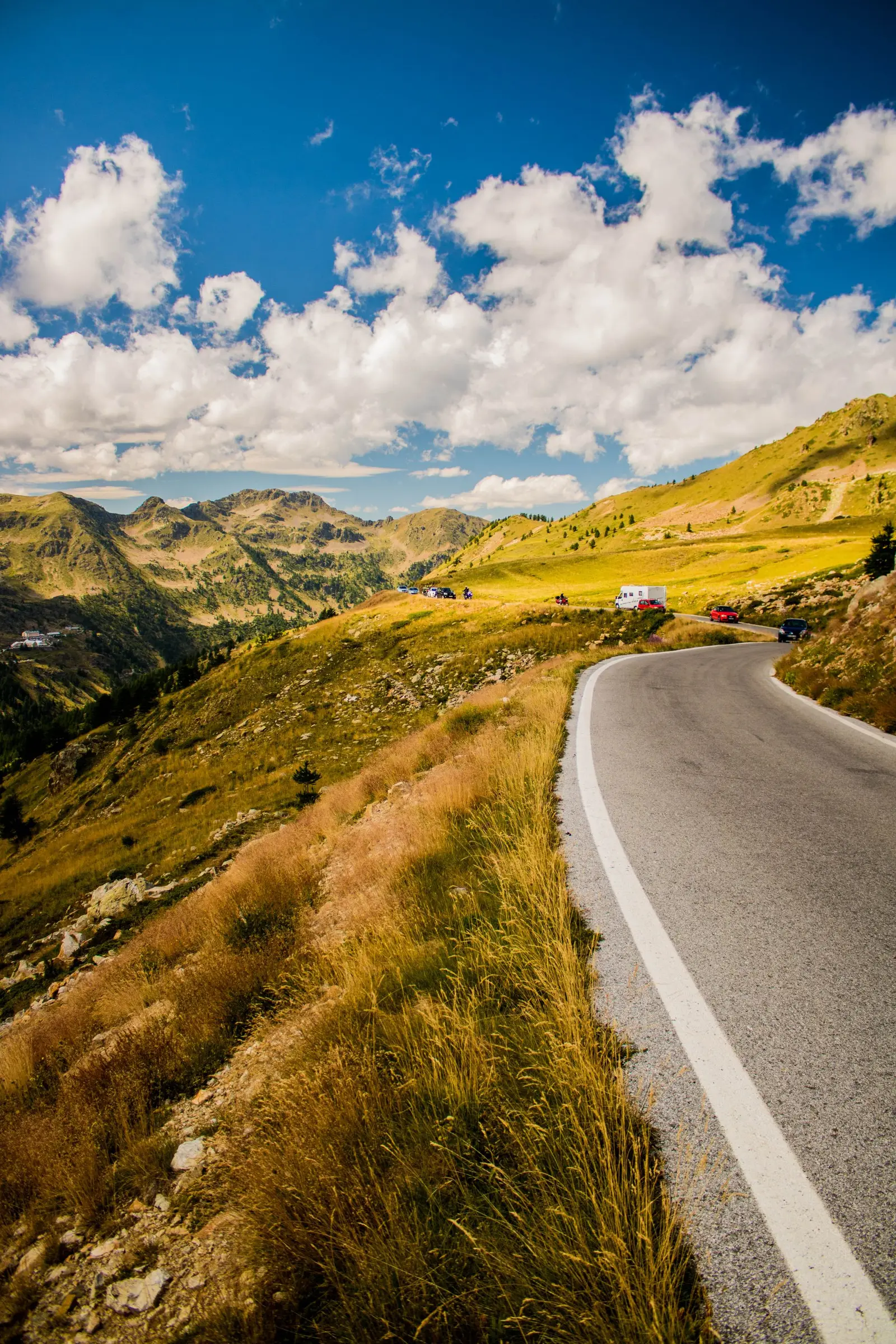 A mountain road curving through open hills, with a few vehicles far ahead
