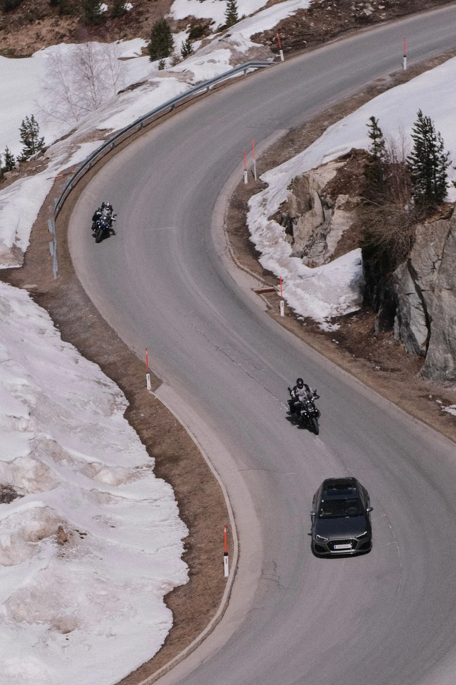 Motorcycles and a car on a hairpin road with snow at the roadside