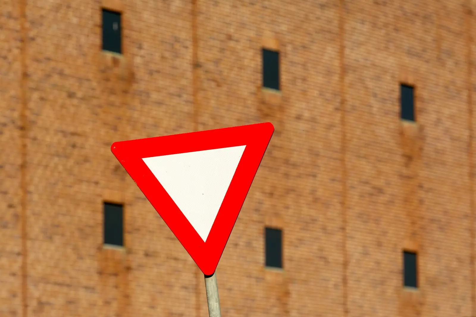 A red-bordered inverted triangle give-way sign against a brick wall