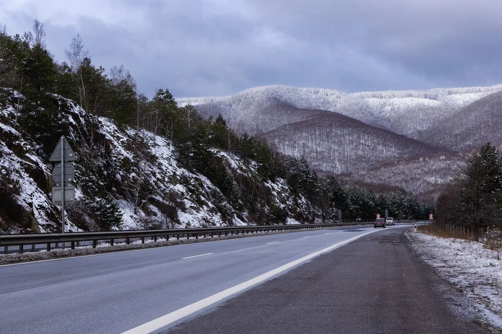 A highway with a damp surface running toward hills dusted with snow